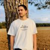 Camiseta Res a demostrar — hombre en el campo Hombre con la camiseta cristiana Res a demostrar en color crudo, apoyado en un pino