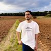 Camiseta Res a demostrar — cuerpo entero Hombre con la camiseta cristiana Res a demostrar de algodón orgánico, de cuerpo entero en un campo